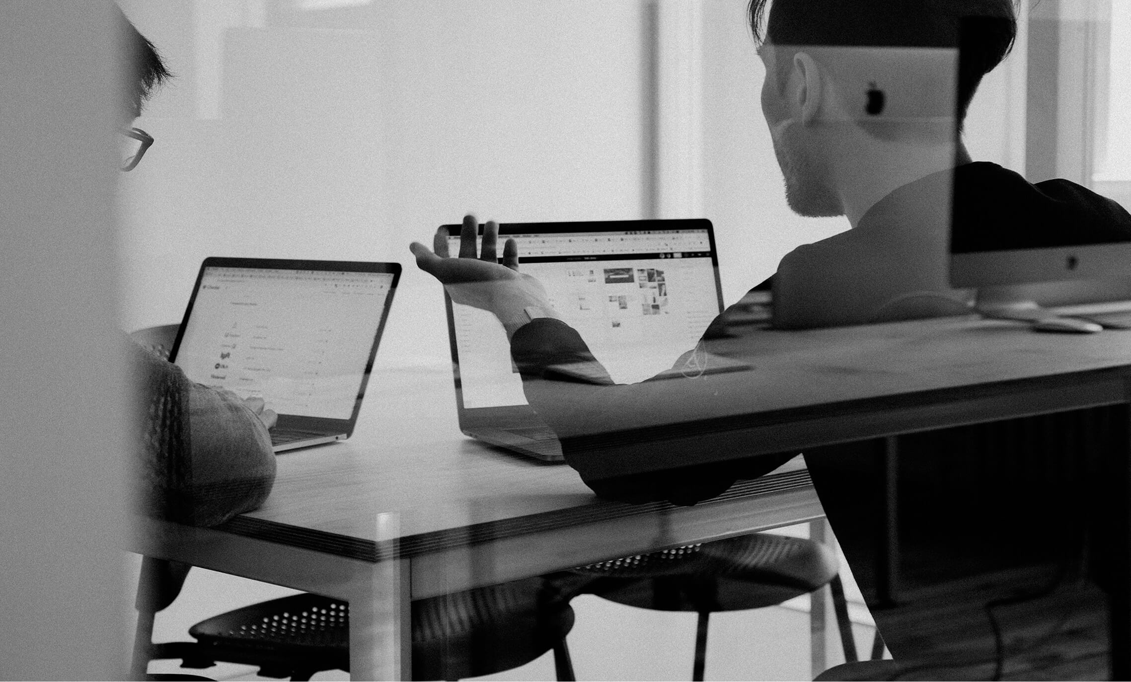 Black and white image of people working at a table with laptops, showing hands gesturing during discussion of digital content displayed on screens, with inara sourcinglogo in the corner.